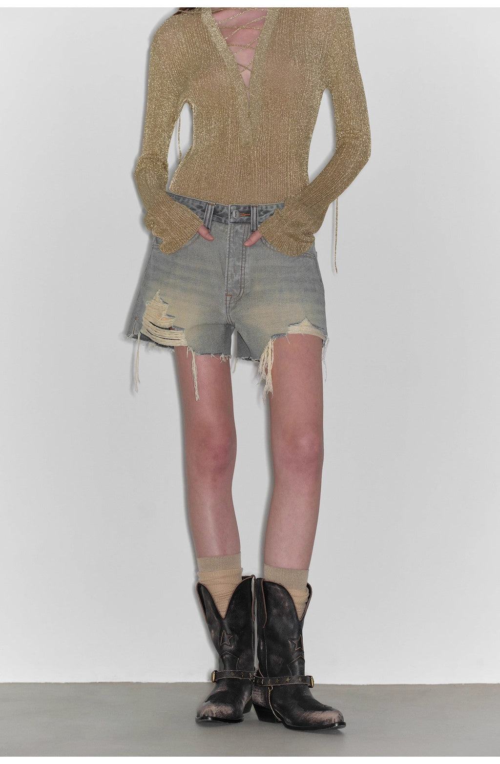Person wearing a brown sweater, denim shorts, and black cowboy boots on a white background