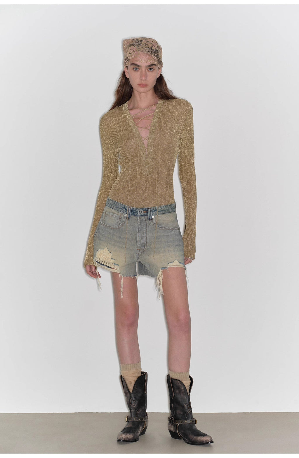 Model wearing a beige sweater, denim shorts, and cowboy boots on a white background