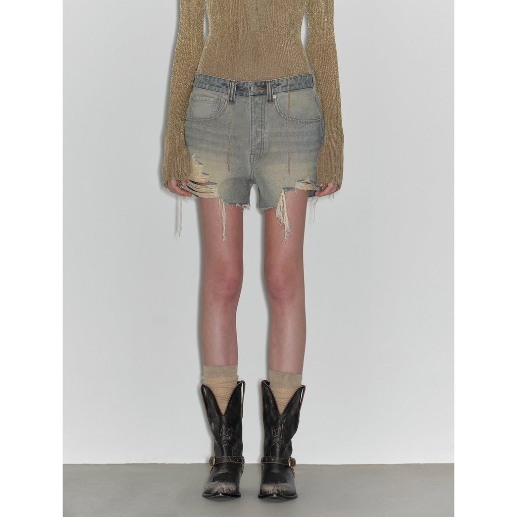 Person wearing distressed denim shorts and black cowboy boots on a plain background
